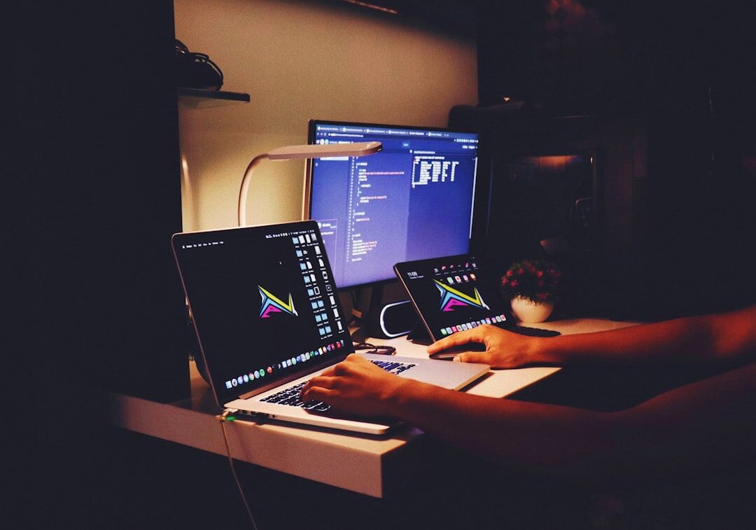 Person typing code on a laptop at a dark desk setup